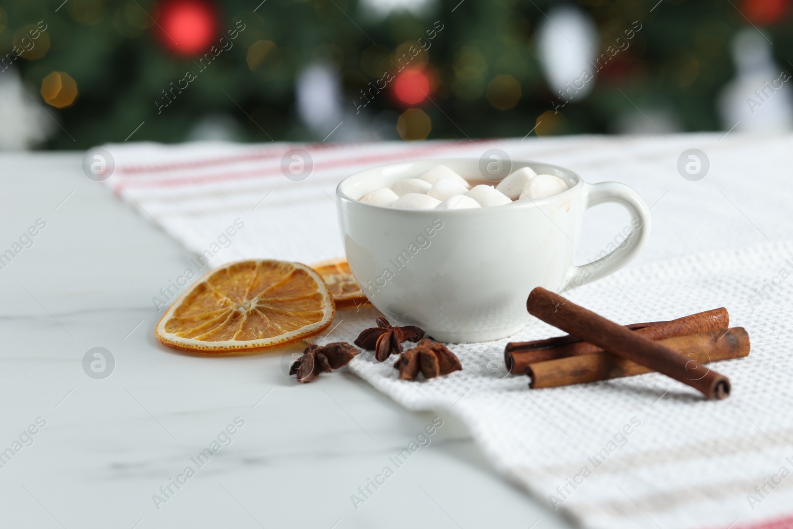 Photo of Tasty hot cocoa drink with marshmallows in cup and spices on white table