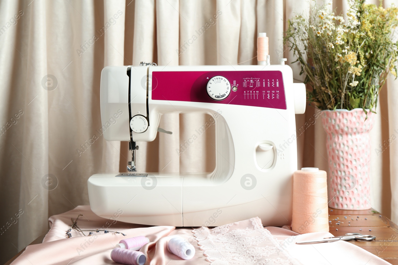 Photo of Sewing machine with fabric, flowers in vase and tools on table indoors