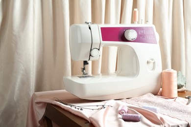 Photo of Sewing machine with fabric and spools on table indoors