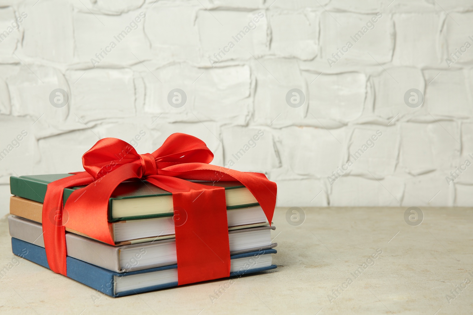 Photo of Stack of books with red ribbon as gift on grey textured table, space for text