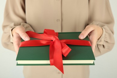 Photo of Woman holding book with ribbon as gift on light background, closeup