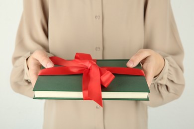 Photo of Woman holding book with ribbon as gift on light background, closeup