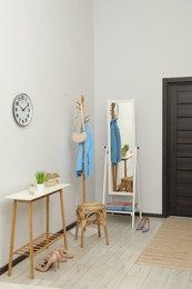 Photo of Clothing rack, mirror, storage bench and clothes in hallway