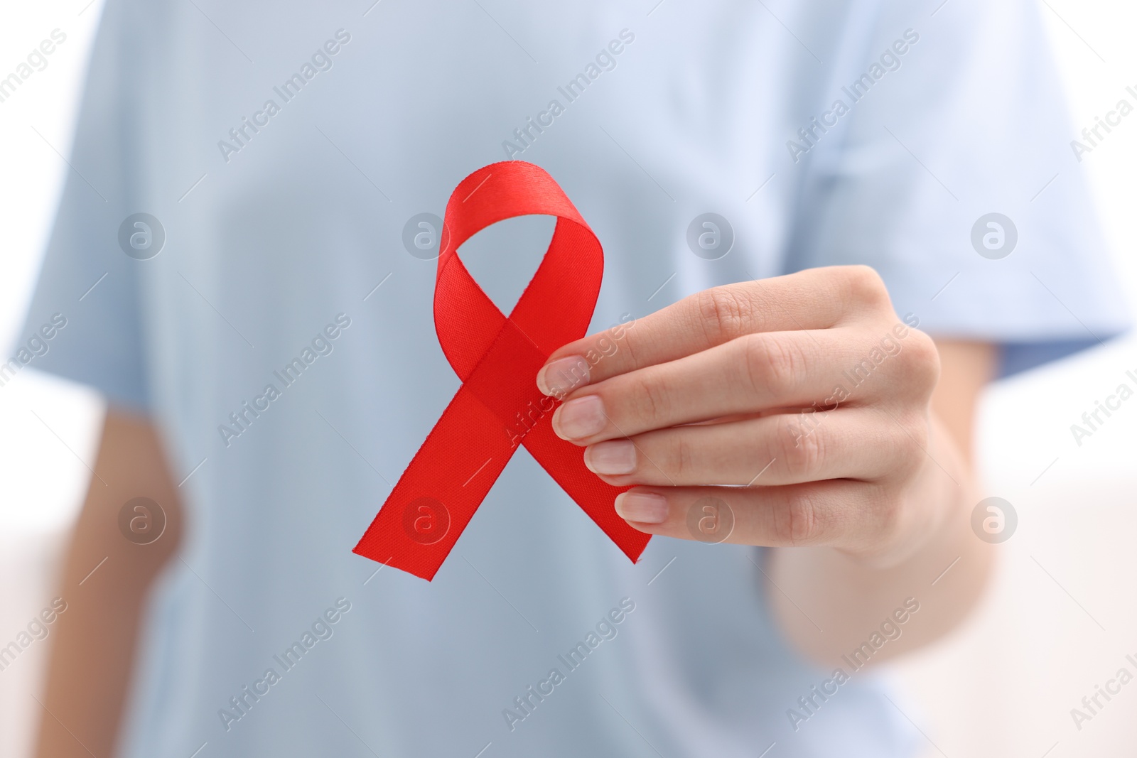 Photo of Woman with red ribbon on light background, closeup. HIV (AIDS) disease awareness