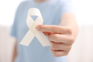 Photo of Woman with white ribbon on light background, closeup. Bone cancer and lung disease awareness