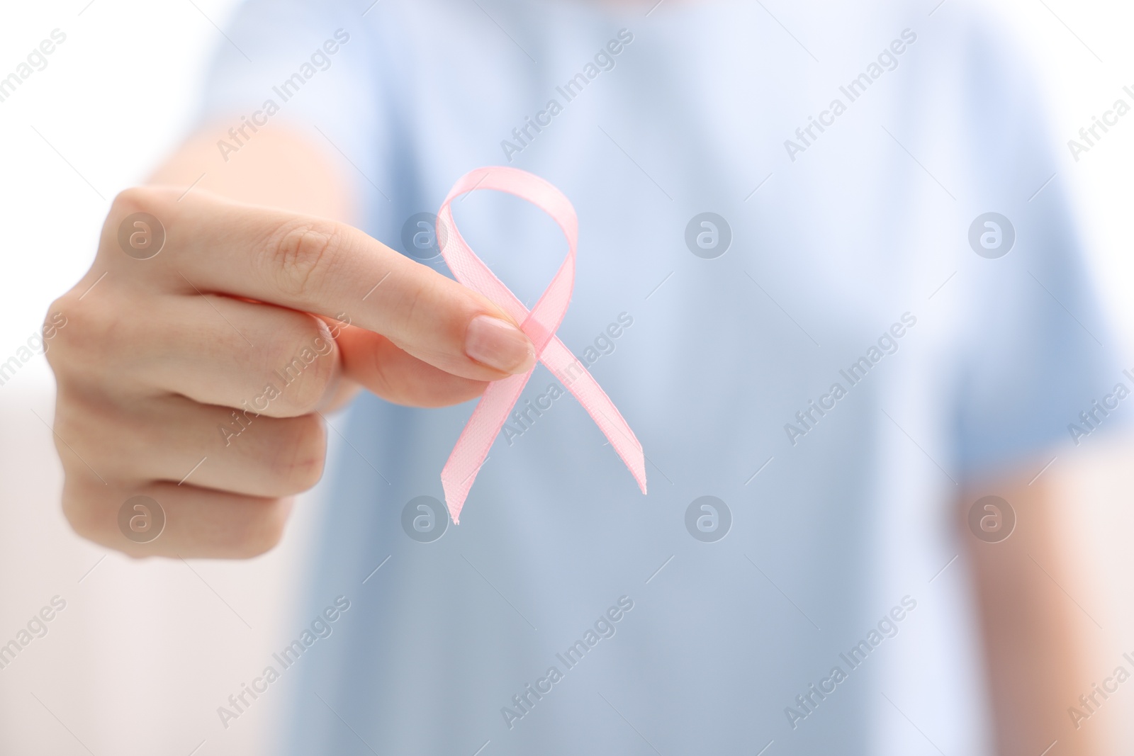 Photo of Woman with pink ribbon on light background, closeup. Breast cancer awareness