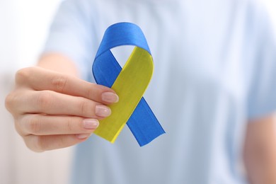 Photo of Woman with yellow and blue ribbon on light background, closeup. Down syndrome awareness