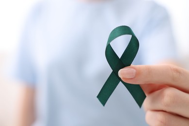 Photo of Woman with teal ribbon on light background, closeup. Ovarian cancer and gynecological disorders awareness