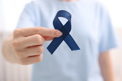 Photo of Woman with dark blue ribbon on light background, closeup. Arthritis disease and colon cancer awareness