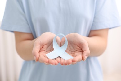 Photo of Woman with light blue ribbon on light background, closeup. Childhood cancer awareness