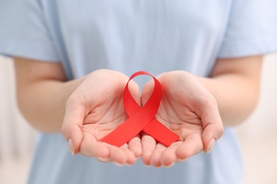 Photo of Woman with red ribbon on light background, closeup. HIV (AIDS) disease awareness