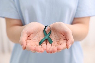 Photo of Woman with teal ribbon on light background, closeup. Ovarian cancer and gynecological disorders awareness