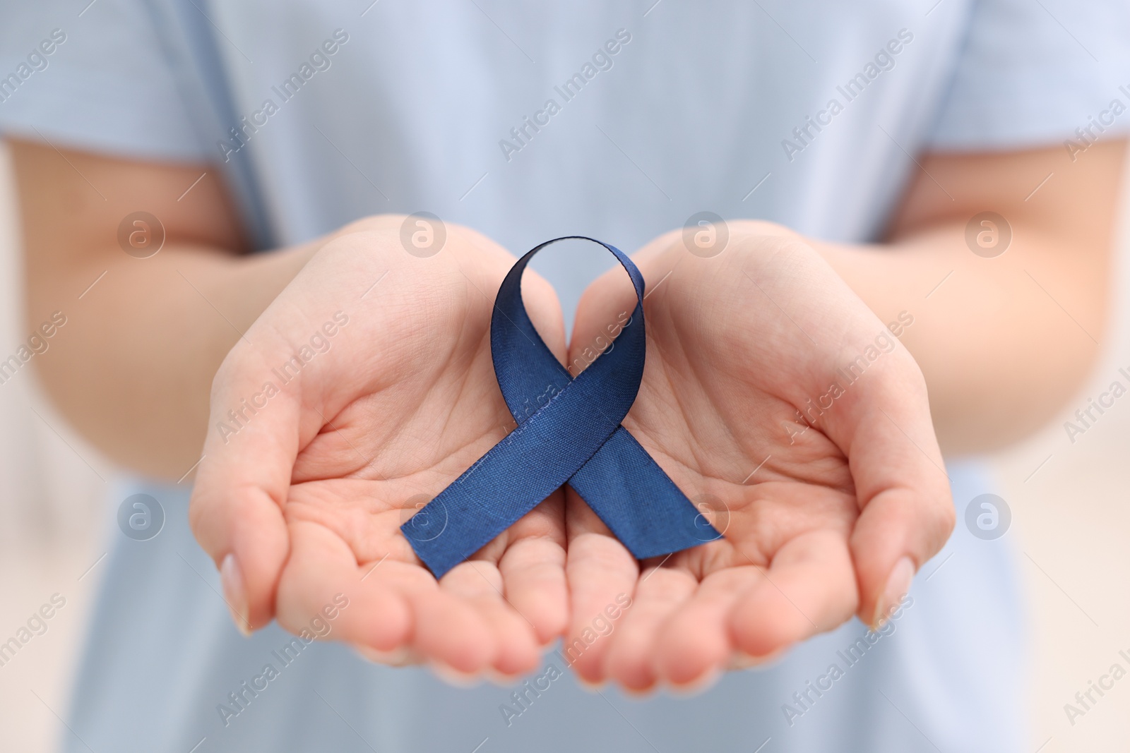 Photo of Woman with dark blue ribbon on light background, closeup. Arthritis disease and colon cancer awareness