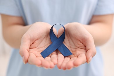 Photo of Woman with dark blue ribbon on light background, closeup. Arthritis disease and colon cancer awareness