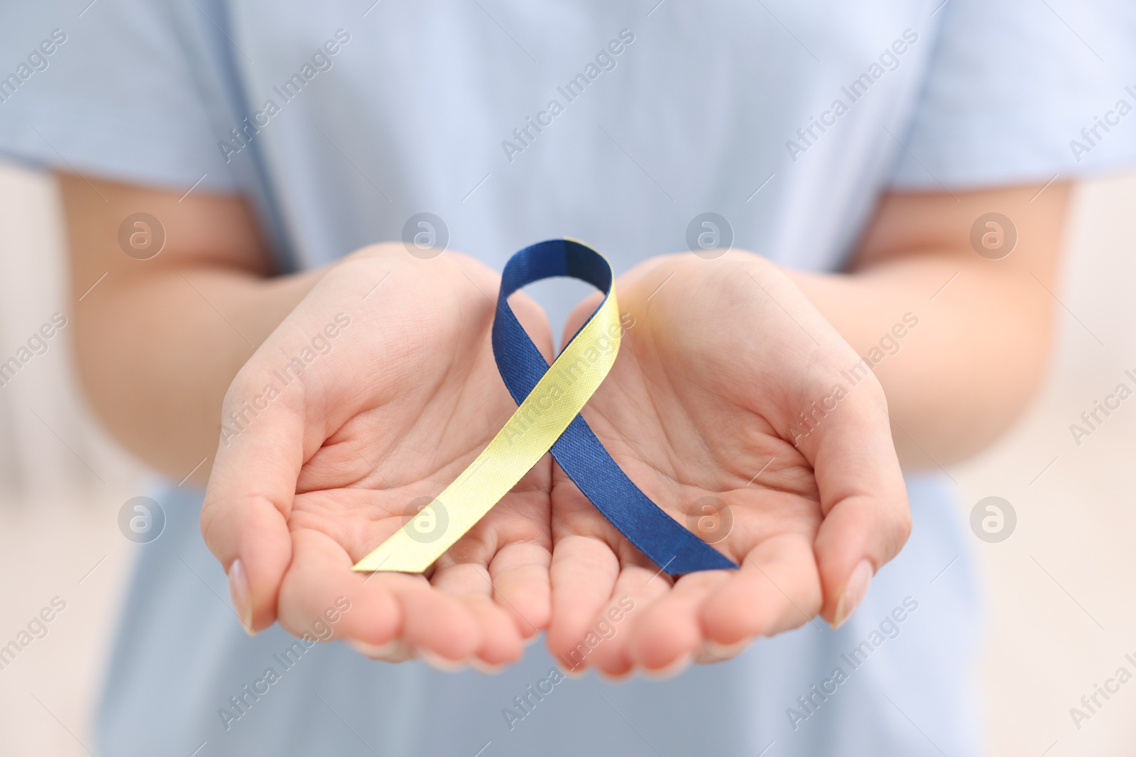 Photo of Woman with yellow and blue ribbon on light background, closeup. Down syndrome awareness