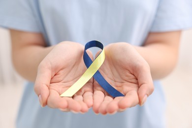 Woman with yellow and blue ribbon on light background, closeup. Down syndrome awareness