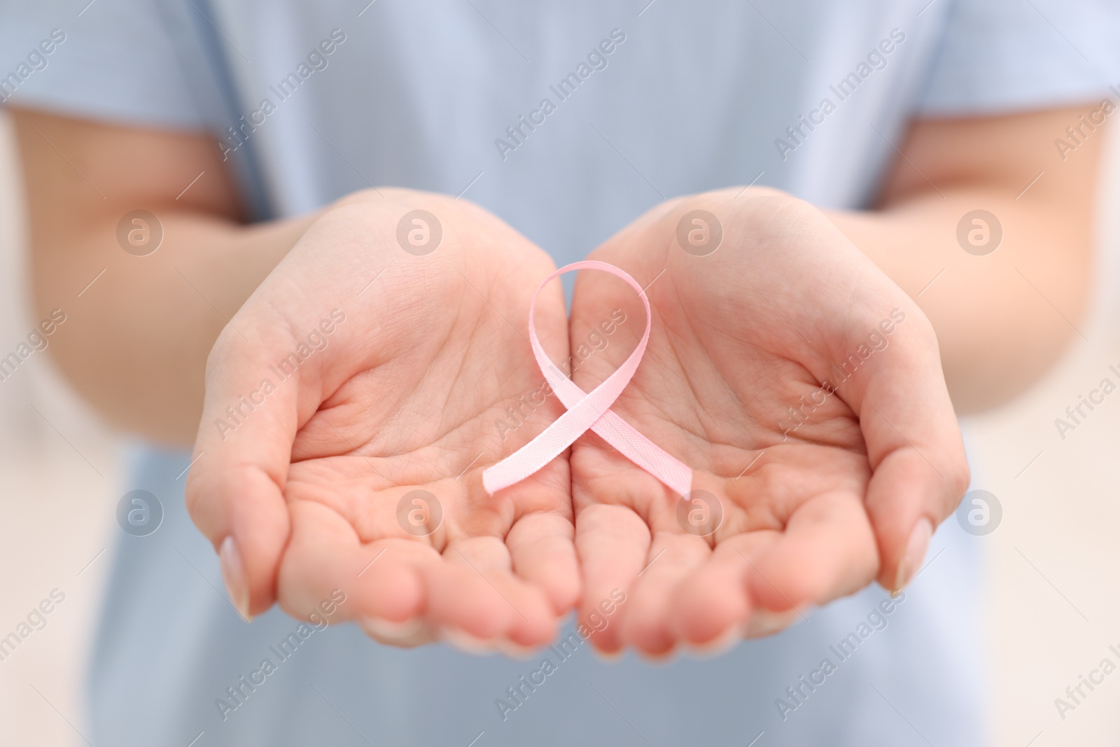 Photo of Woman with pink ribbon on light background, closeup. Breast cancer awareness