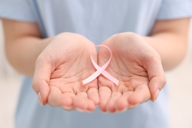 Photo of Woman with pink ribbon on light background, closeup. Breast cancer awareness