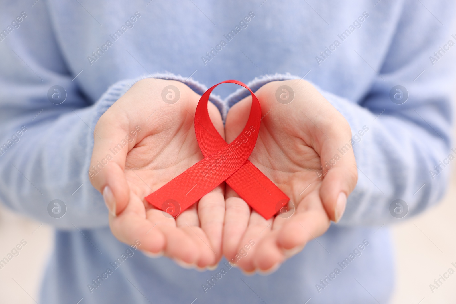 Photo of Woman with red ribbon on light background, closeup. HIV (AIDS) disease awareness