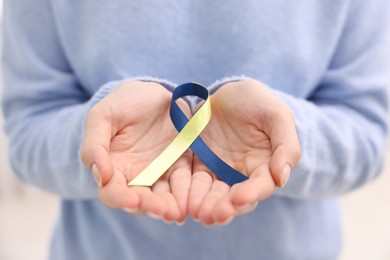 Photo of Woman with yellow and blue ribbon on light background, closeup. Down syndrome awareness