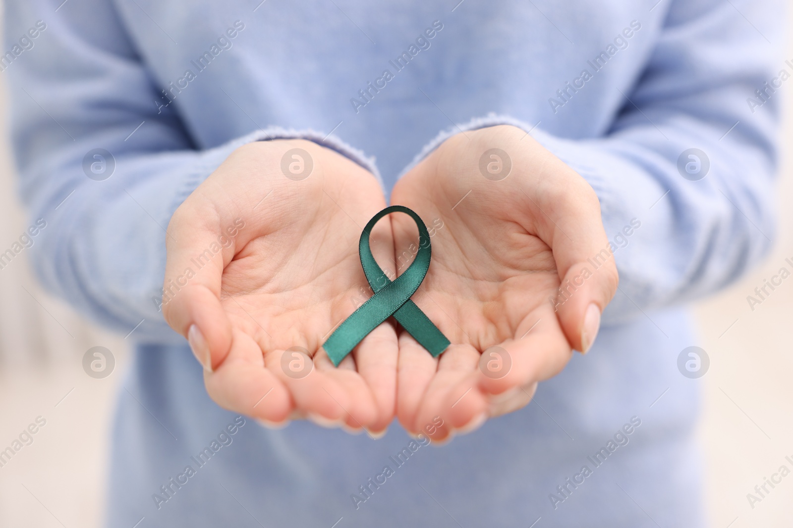 Photo of Woman with teal ribbon on light background, closeup. Ovarian cancer and gynecological disorders awareness