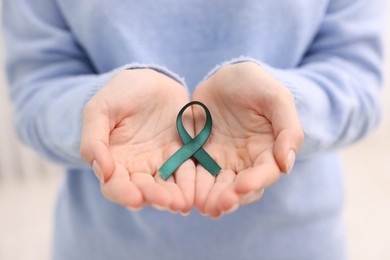 Photo of Woman with teal ribbon on light background, closeup. Ovarian cancer and gynecological disorders awareness