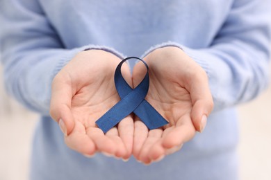 Photo of Woman with dark blue ribbon on light background, closeup. Arthritis disease and colon cancer awareness