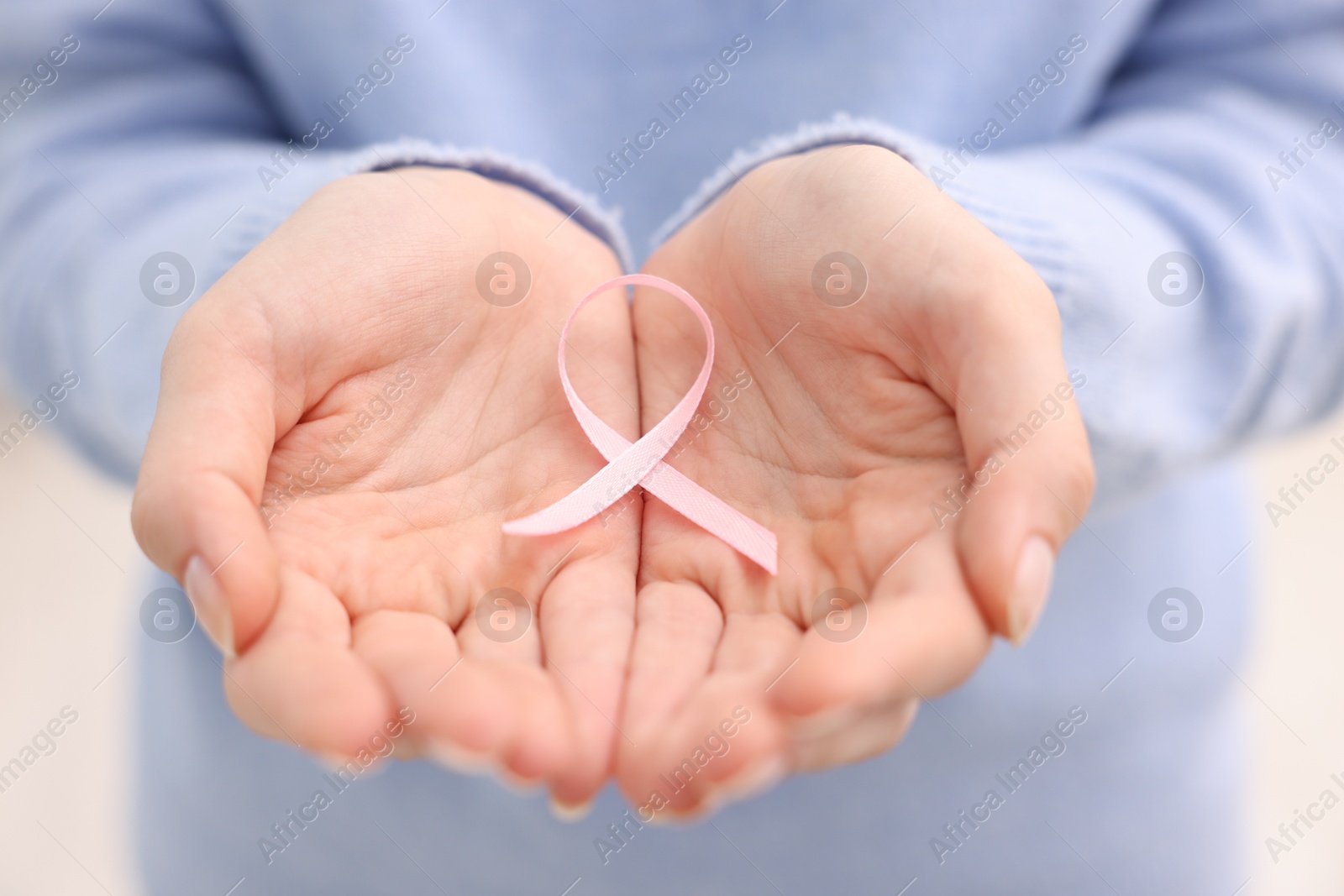 Photo of Woman with pink ribbon on light background, closeup. Breast cancer awareness