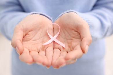 Photo of Woman with pink ribbon on light background, closeup. Breast cancer awareness