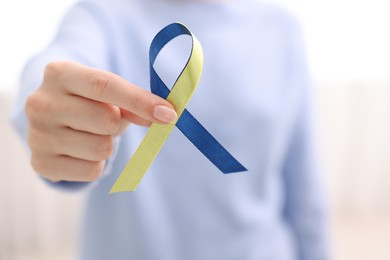 Photo of Woman with yellow and blue ribbon on light background, closeup. Down syndrome awareness