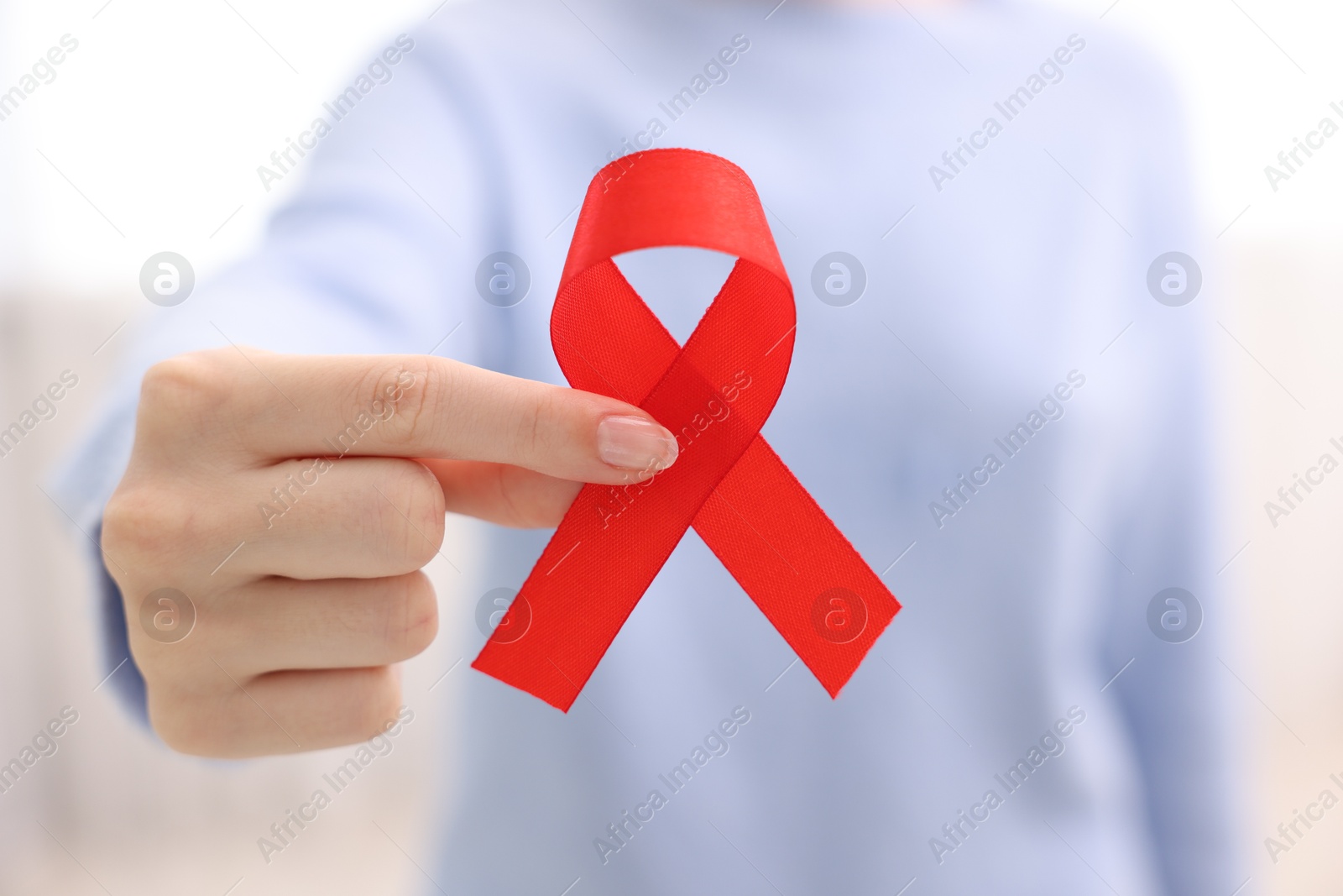 Photo of Woman with red ribbon on light background, closeup. HIV (AIDS) disease awareness