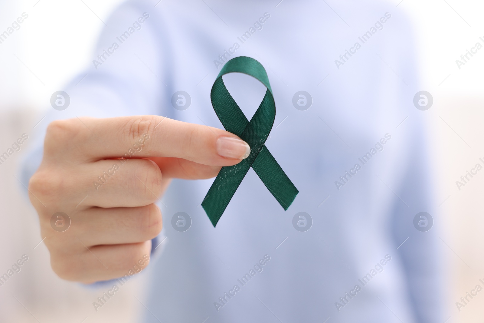 Photo of Woman with teal ribbon on light background, closeup. Ovarian cancer and gynecological disorders awareness