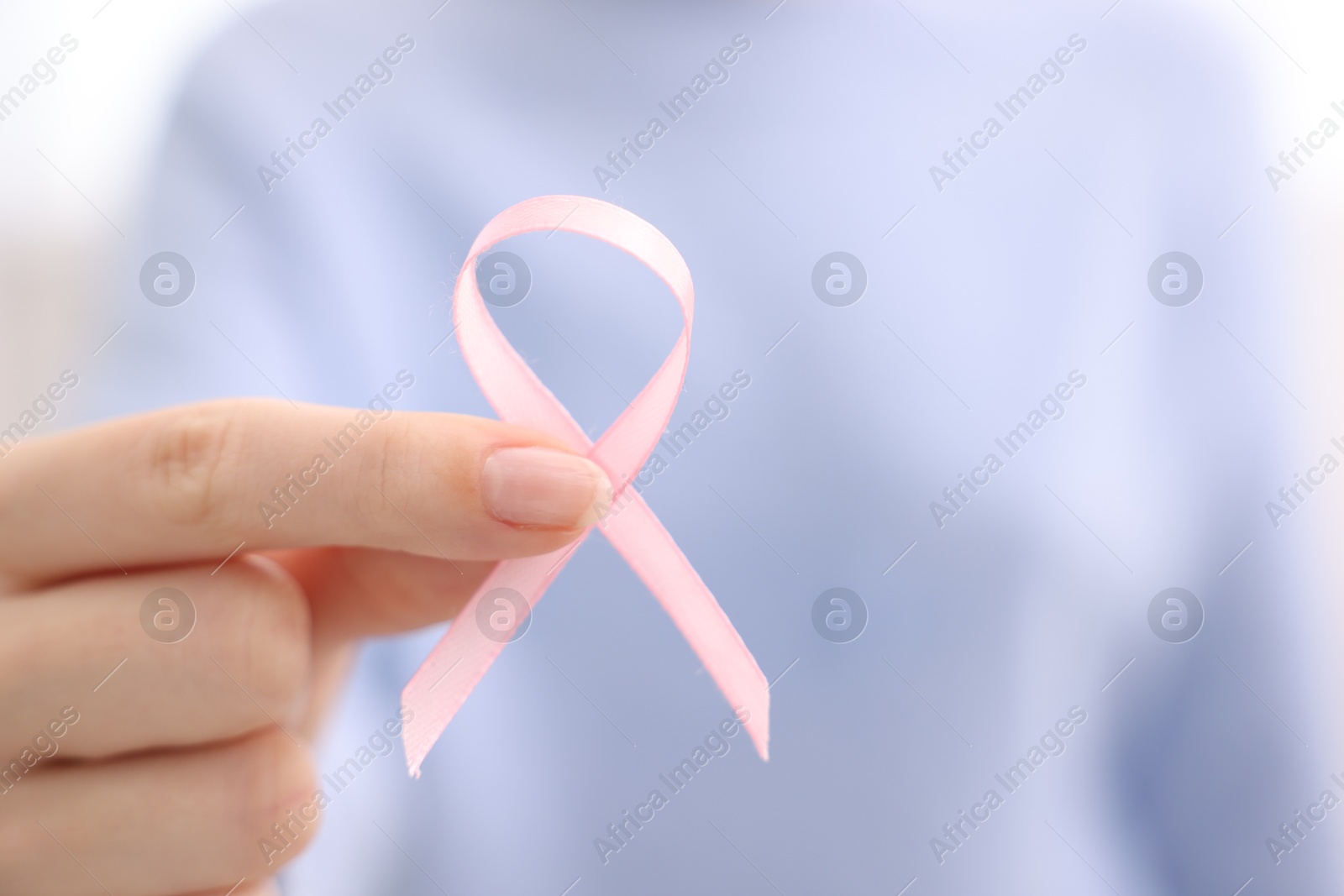 Photo of Woman with pink ribbon on light background, closeup with space for text. Breast cancer awareness