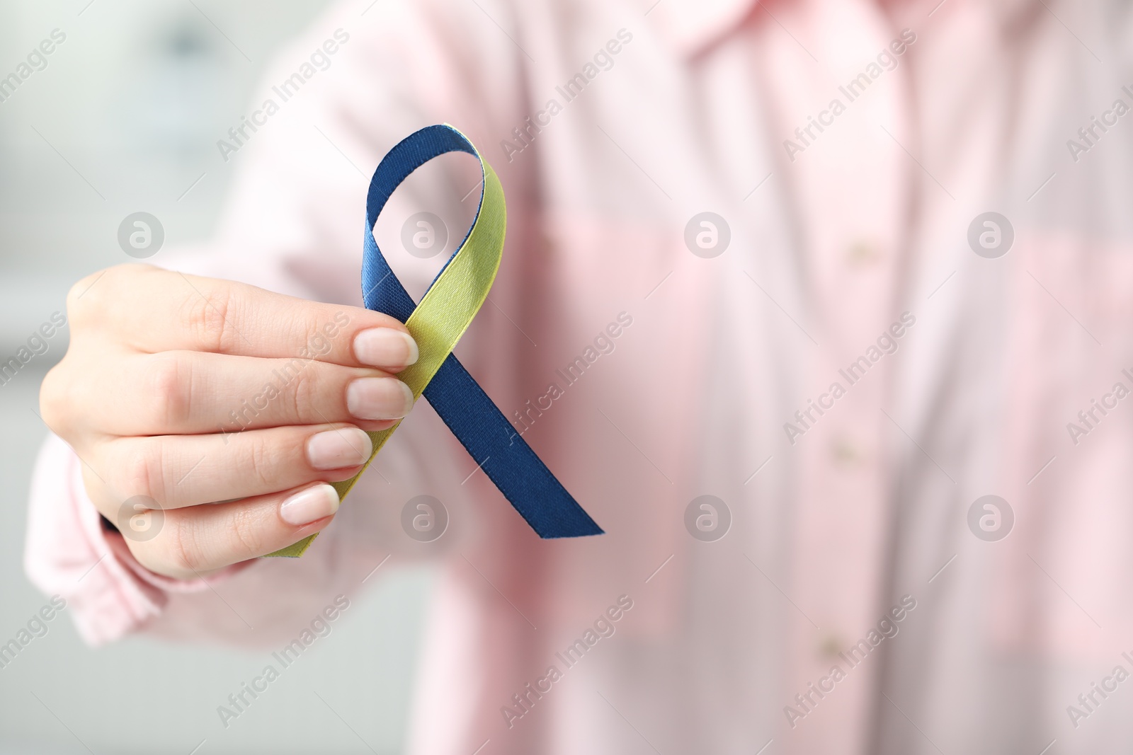 Photo of Woman with yellow and blue ribbon on light background, closeup. Down syndrome awareness