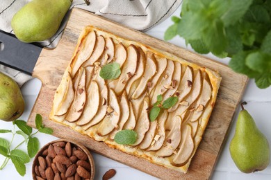 Photo of Delicious puff pastry tart with pears, almond and mint on light tiled table, flat lay