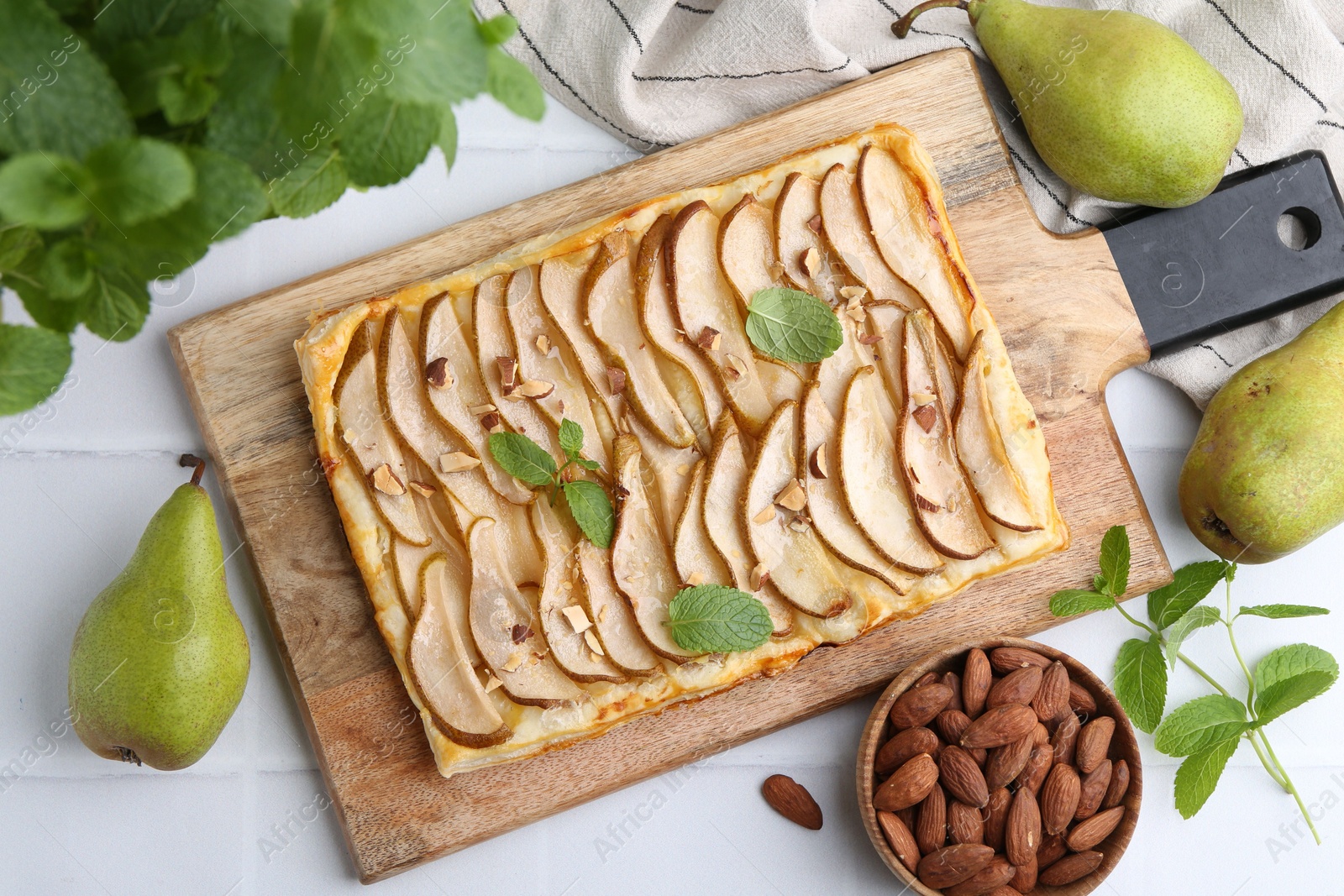 Photo of Delicious puff pastry tart with pears, almond and mint on light tiled table, flat lay