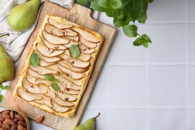 Delicious puff pastry tart with pears, almond and mint on light tiled table, flat lay. Space for text