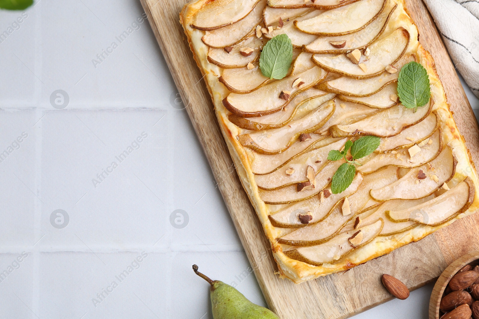 Photo of Delicious puff pastry tart with pears, almond and mint on light tiled table, flat lay. Space for text