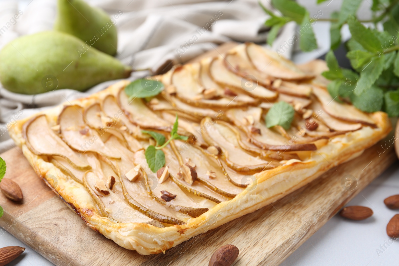 Photo of Delicious puff pastry tart with pears, almond and mint on light table, closeup