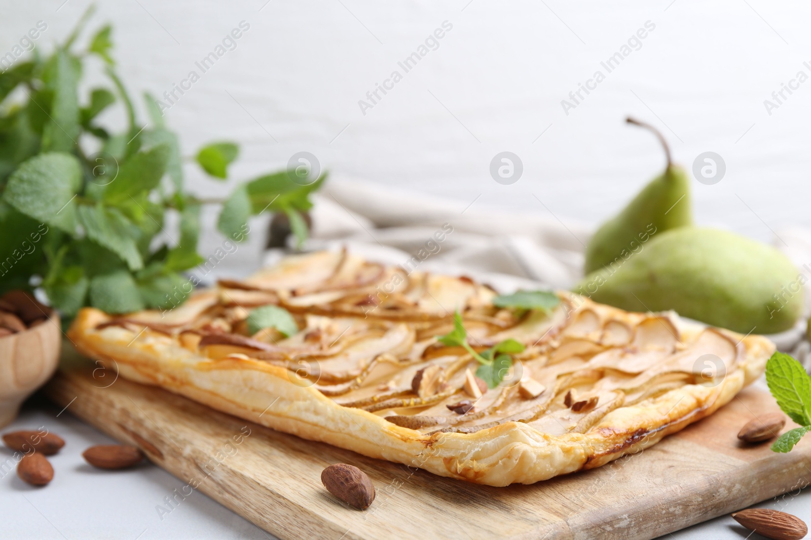 Photo of Delicious puff pastry tart with pears, almond and mint on light table, closeup