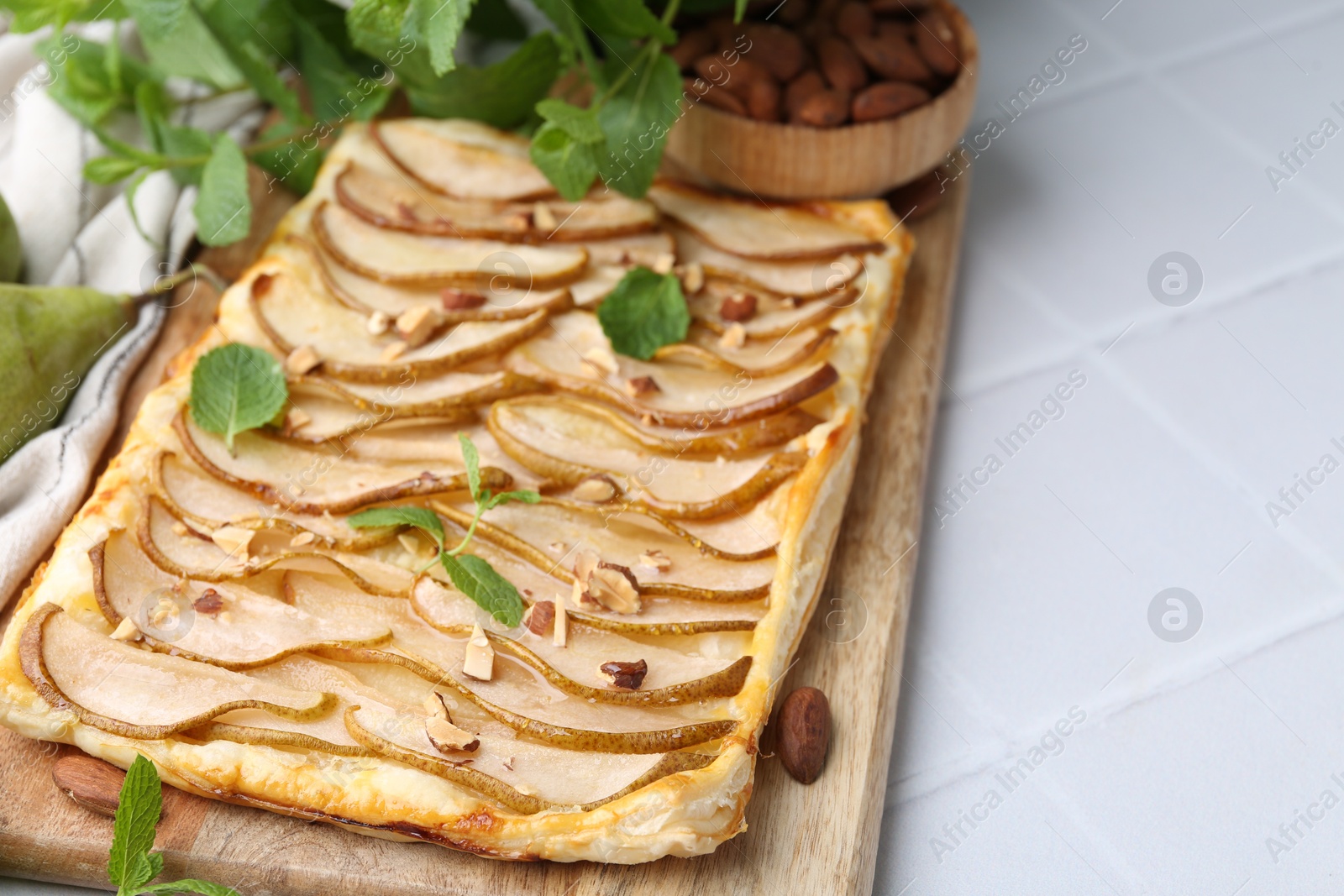 Photo of Delicious puff pastry tart with pears, almond and mint on light tiled table, closeup. Space for text