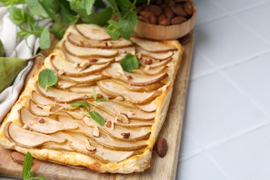 Delicious puff pastry tart with pears, almond and mint on light tiled table, closeup. Space for text