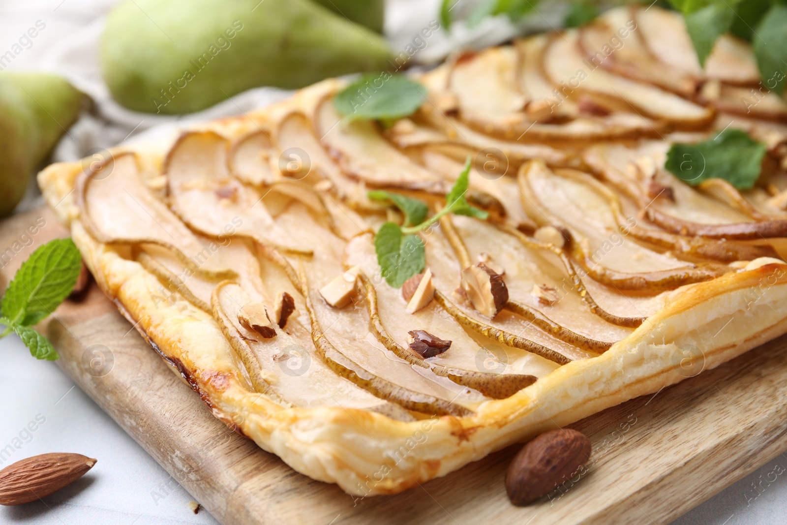 Photo of Delicious puff pastry tart with pears, almond and mint on light table, closeup