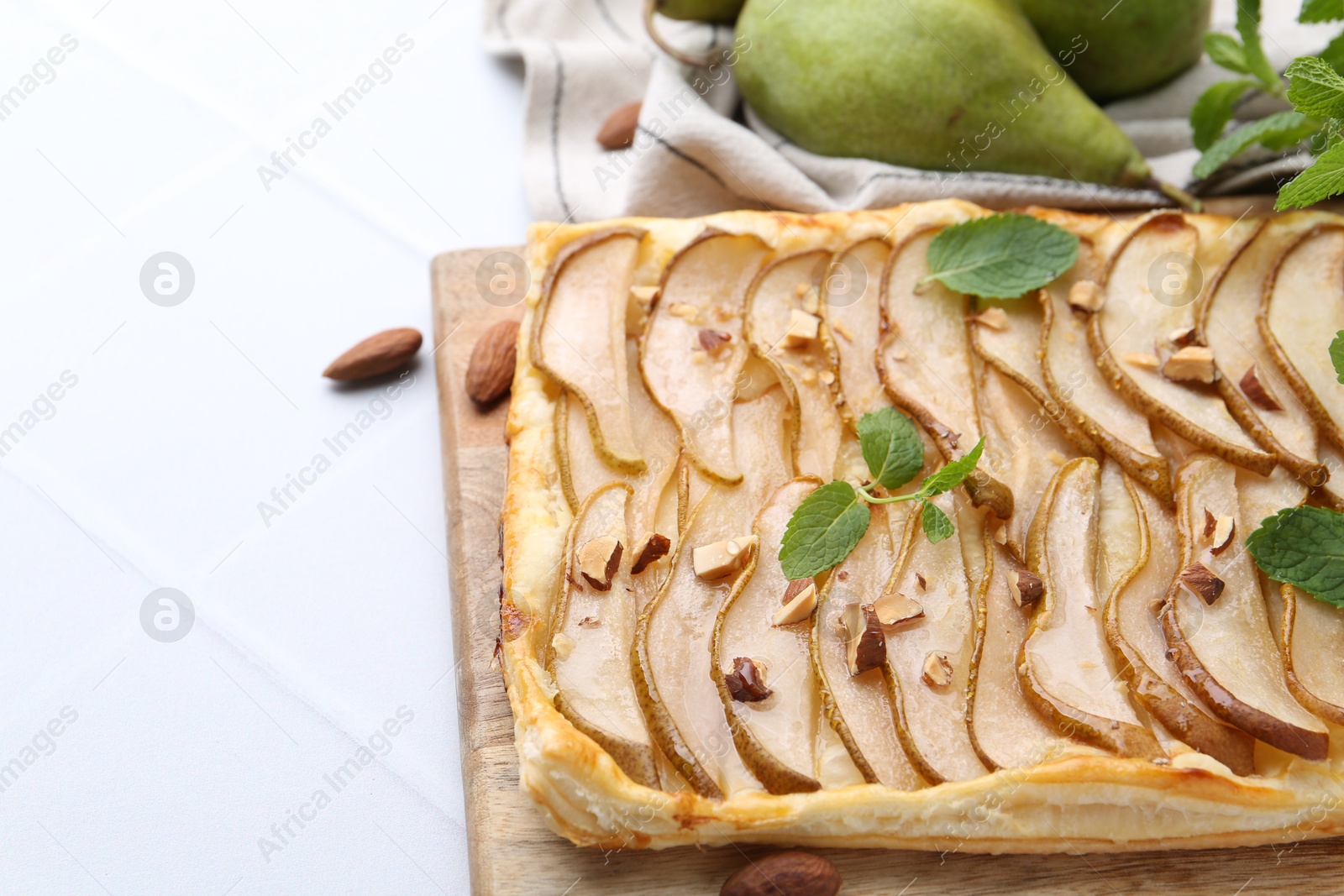 Photo of Delicious puff pastry tart with pears, almond and mint on light tiled table, above view. Space for text