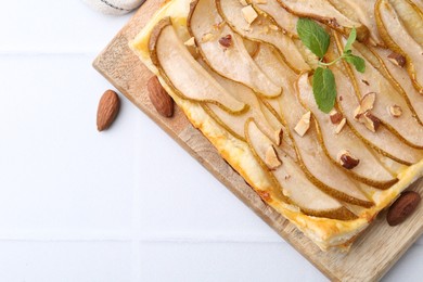 Photo of Delicious puff pastry tart with pears, almond and mint on light tiled table, top view. Space for text