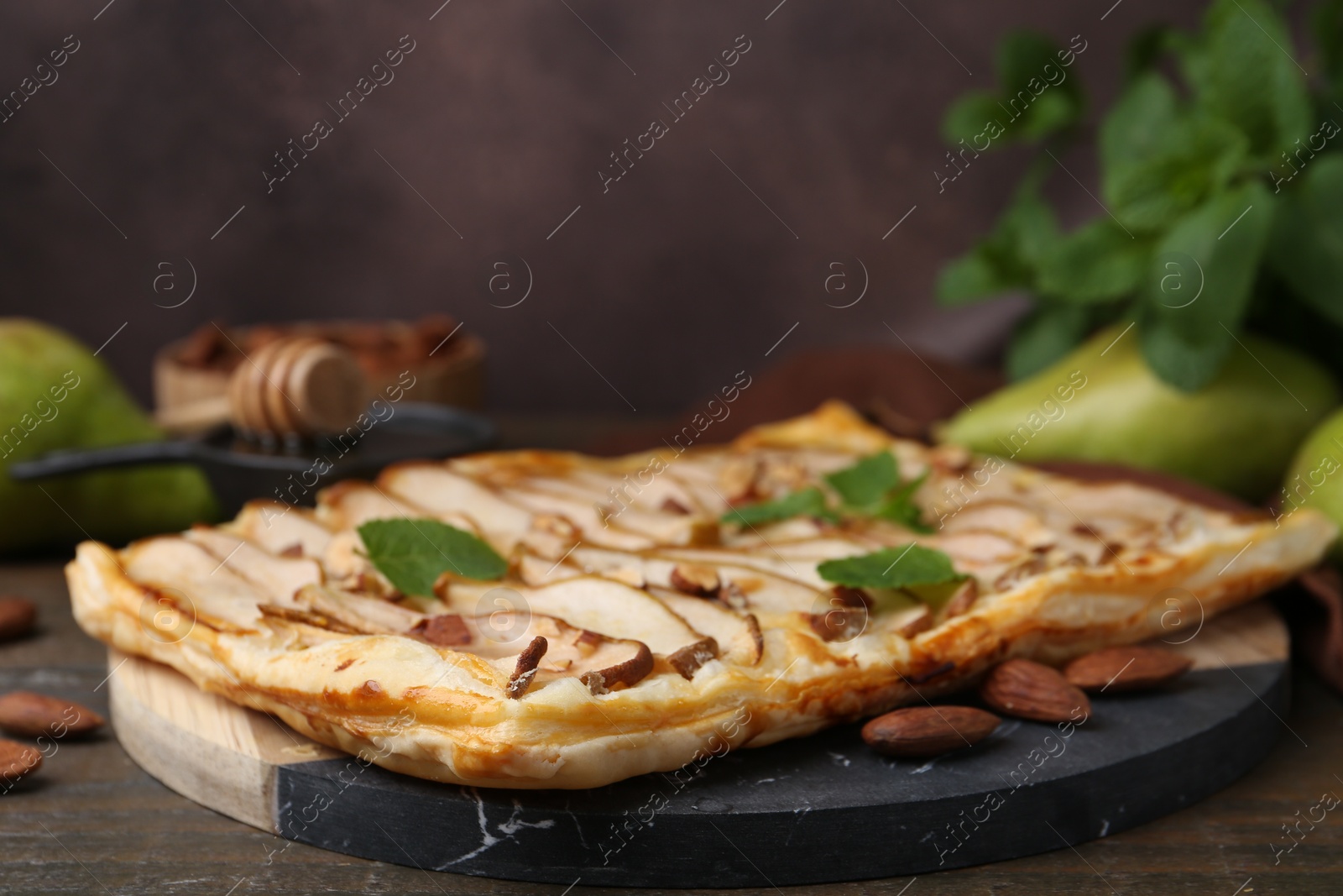 Photo of Delicious puff pastry tart with pears, almond and mint on wooden table, closeup