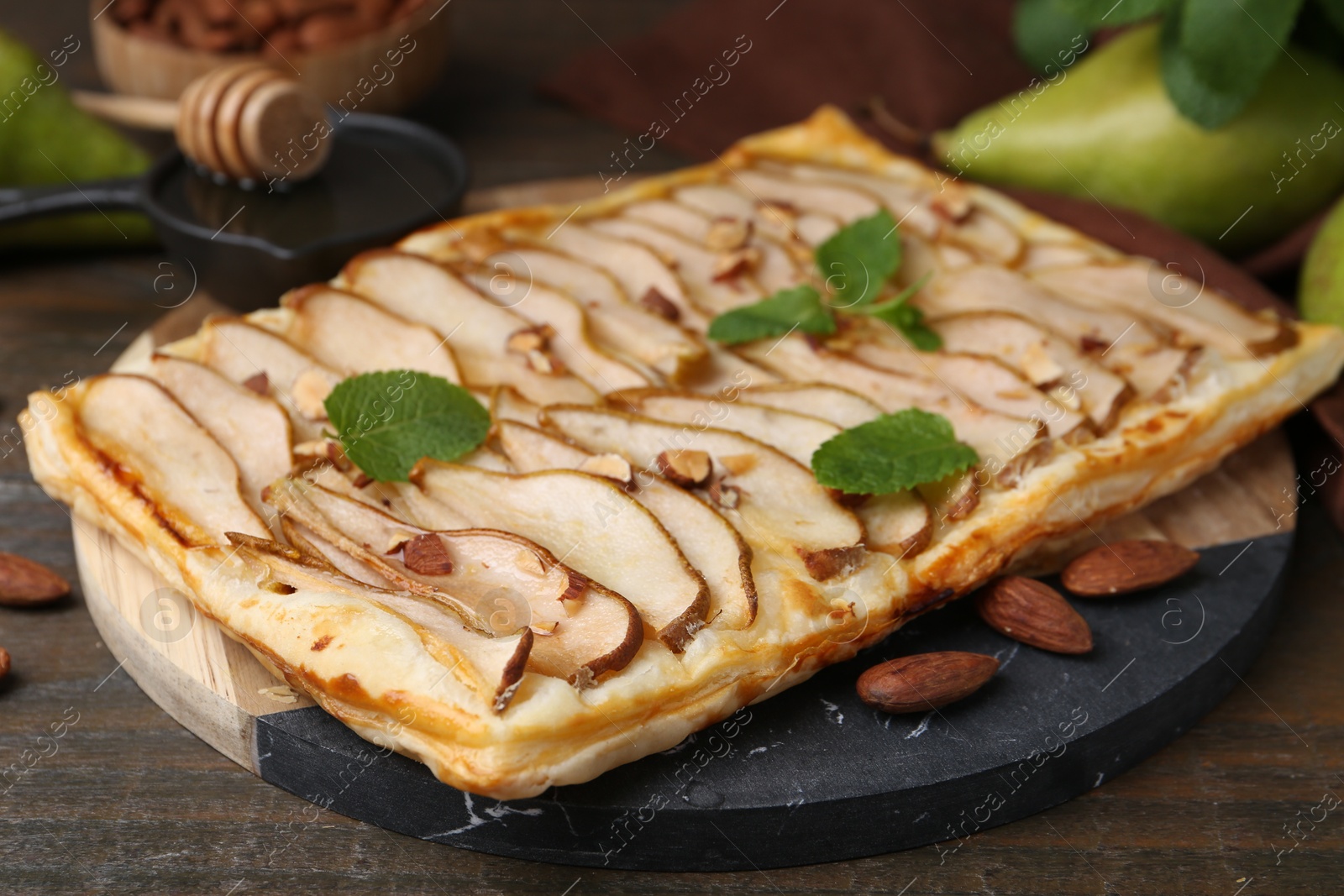 Photo of Delicious puff pastry tart with pears, almond and mint on wooden table, closeup