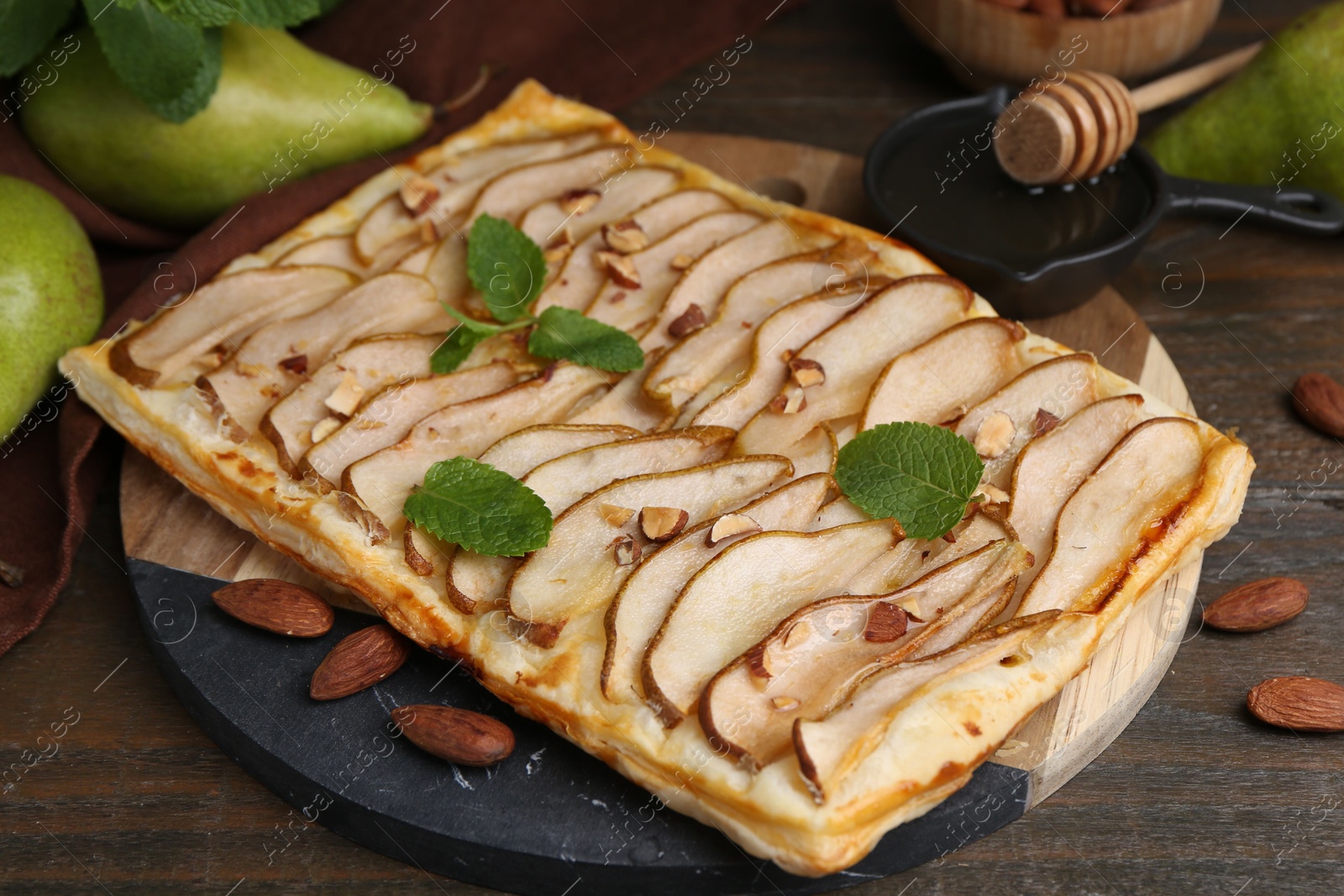 Photo of Delicious puff pastry tart with pears, almond and mint on wooden table, closeup