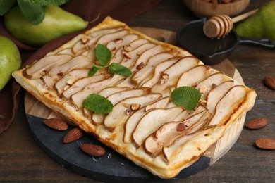 Photo of Delicious puff pastry tart with pears, almond and mint on wooden table, closeup