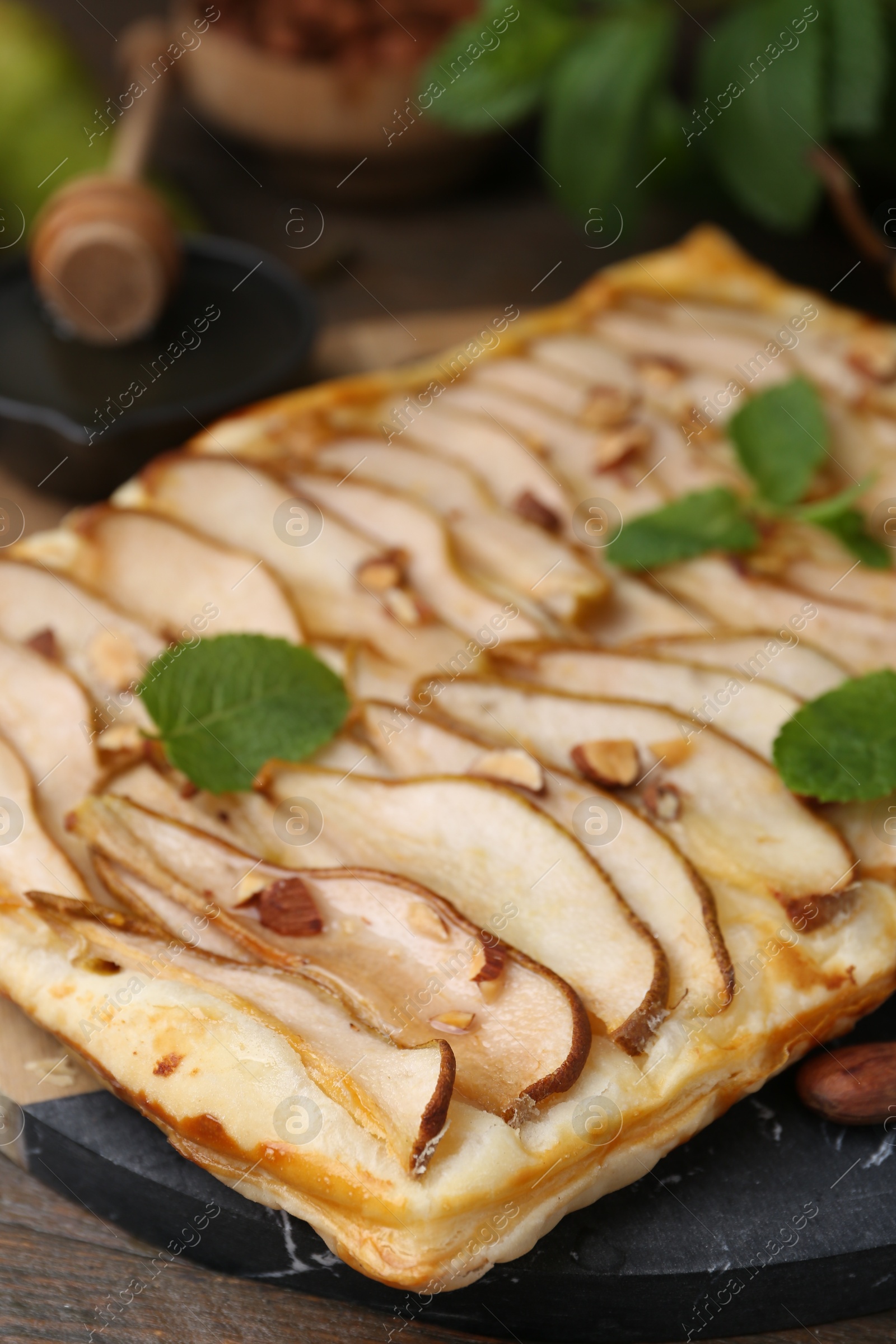 Photo of Delicious puff pastry tart with pears, almond and mint on wooden table, closeup